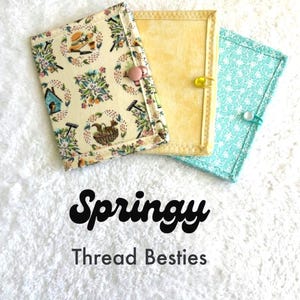 May include: Three fabric thread organizers. One is cream-coloured with a floral and gardening-themed pattern, secured with a pink button. The second is yellow, and the third is light blue with a white floral pattern, both secured with pins. The text "Springy Thread Besties" is below.