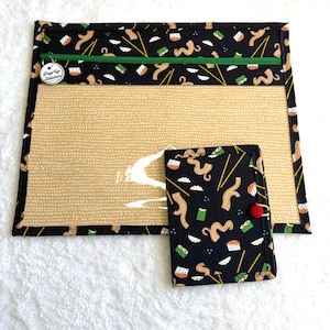 Può includere: Un astuccio con cerniera nero e beige e un piccolo portafoglio abbinato. Entrambi gli articoli presentano un motivo ripetuto di noodles, sushi e bacchette. L'astuccio ha un fronte trasparente e una cerniera verde. Il portafoglio ha una chiusura con bottone rosso.