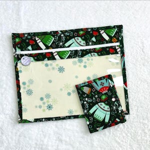 Può includere: Un set di due pochette in tessuto con un motivo festivo natalizio. La pochette più grande ha una finestra trasparente e una cerniera bianca. La pochette più piccola è un accessorio abbinato. Il motivo include maglioni, fiocchi di neve e tazze su sfondo verde scuro.