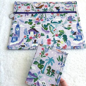 Può includere: Un organizer in tessuto lavanda e una piccola copertina per quaderno abbinata. Entrambi gli articoli presentano una stampa stravagante con illustrazioni di una nave, una torre dell'orologio e scene tropicali. L'organizer ha una cerniera viola.