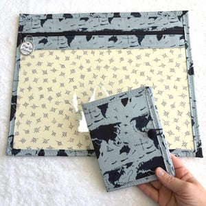Può includere: Un set di organizer a tema viaggio blu chiaro e blu navy. Il set include una grande custodia con cerniera e un piccolo portafoglio. La custodia ha una finestra trasparente con sfondo color crema e motivo a stelle. Un portafoglio è tenuto da una mano.