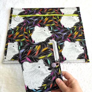 Può includere: Un set di tessuti in bianco e nero con un motivo di orso bianco e accenti di foglie colorate. Il set include una pochette con cerniera e una copertina per notebook con chiusura a bottone. Il tessuto ha un motivo ripetuto.