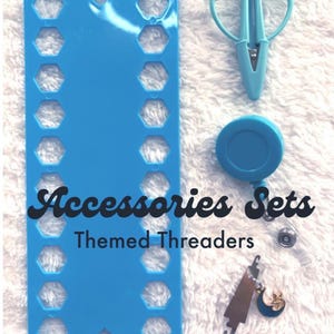 May include: A light blue plastic thread organizer with hexagonal cutouts, a light blue pair of embroidery scissors, a retractable badge reel, and a metal needle threader with a small moon charm. The text reads Accessories Sets Themed Threaders.