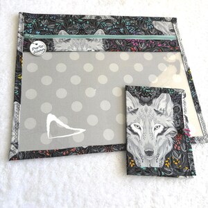 Può includere: Una borsa per progetti Pop Up Stitcher grigia e nera e un portafoglio abbinato. La borsa presenta una finestra trasparente con pois bianchi e una chiusura a cerniera. Il tessuto ha un motivo a lupo e floreale. Il portafoglio ha una faccia di lupo.