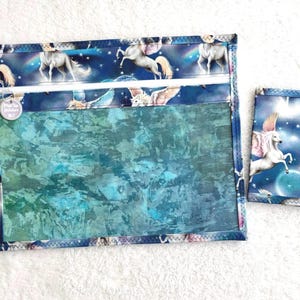 Può includere: Set di due pochette in tessuto. La pochette più grande ha un fronte trasparente e una chiusura con cerniera. La parte superiore e inferiore sono decorate con tessuto blu con unicorni bianchi. La pochette più piccola ha una grafica di unicorno.