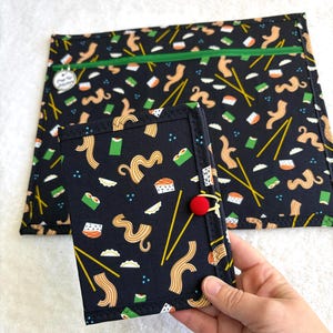 Può includere: Set di tessuto nero con motivo sushi e noodle. Il set include una pochette con cerniera e un piccolo astuccio tipo taccuino con chiusura a bottone rosso. Il design presenta bacchette gialle, sushi e noodle.