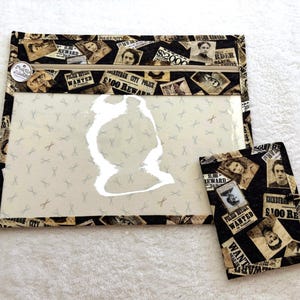 May include: A rectangular zippered pouch and a smaller matching folded case, both featuring a black and beige fabric print of vintage wanted posters and police notices. The pouch has a clear vinyl front panel with a small scissor pattern.