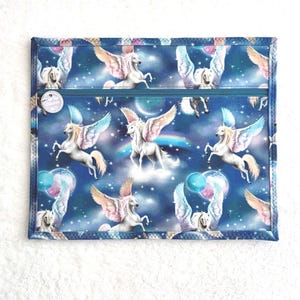 Può includere: Un astuccio rettangolare in tessuto blu con chiusura a cerniera. L'astuccio è decorato con un motivo di cavalli Pegaso bianchi con ali rosa e blu, su uno sfondo di cielo stellato. L'astuccio ha un'etichetta bianca con testo.