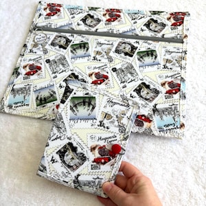 Può includere: Un set di tessuto bianco con una grande pochette con cerniera e un portafoglio più piccolo. Entrambi gli articoli sono ricoperti da un motivo ripetuto di disegni di francobolli con illustrazioni e testo tra cui "Hogwarts Express" e "Quidditch Pitch". Il portafoglio ha una chiusura a bottone rosso.