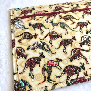 Può includere: Un astuccio rettangolare con sfondo color crema con un motivo di canguri stilizzati in vari colori. I canguri presentano intricati disegni in rosso, verde e nero. Una cerniera bordeaux e un'etichetta metallica con la scritta "Pop Up Stitcher" sono visibili.