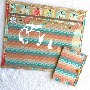 Può includere: Un set di due pochette in tessuto. La pochette più grande ha un fronte trasparente con un motivo a onde in corallo, verde acqua e oro. La parte superiore presenta una cerniera e un motivo a capanne sulla spiaggia. La pochette più piccola ha un motivo a onde abbinato e una chiusura con bottone giallo.