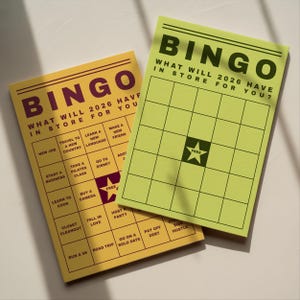 May include: Two bingo cards with the word "BINGO" at the top. The cards are yellow and green with black grid lines and text. The text on the cards reads "WHAT WILL 2026 HAVE IN STORE FOR YOU?" and includes various activity prompts.