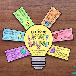 以下が含まれることがあります： LET YOUR LIGHT SHINEという文字が書かれた黄色い電球の形をしたペーパークラフト。周囲には6枚のカラフルな長方形のタブが付いており、それぞれに手書きのプロンプトと、スマイリーフェイス、ハート、地球儀などのイラストが描かれています。