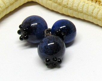 May include: Three dark blue glass beads with black accents, resembling blueberries.