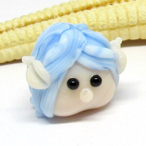 May include: A small glass figurine with a white face, blue hair, and white ears. The figurine has black eyes and a small white nose.
