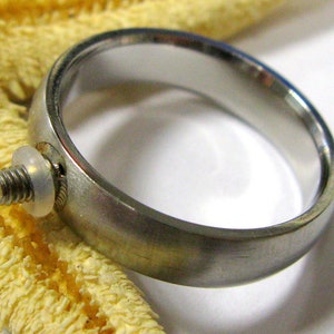 Peut inclure: Une bague en argent avec une petite vis et une rondelle en plastique transparente fixée sur le côté.