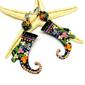 Könnte beinhalten: Ein Paar schwarze Hängeohrringe mit einem floralen Design. Die Ohrringe sind aus Polymer Clay gefertigt und in verschiedenen Farben gehalten, darunter Pink, Lila, Orange und Gelb. Die Ohrringe hängen an silbernen Haken.