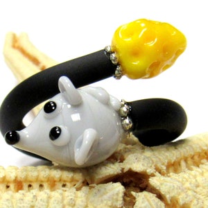 May include: A grey glass mouse charm with black eyes and a yellow glass bead charm on a black elastic band.