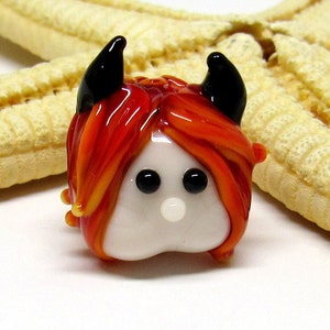 May include: A small glass figurine of a red-haired devil with black horns and white eyes. The figurine is made of glass and has a white face.