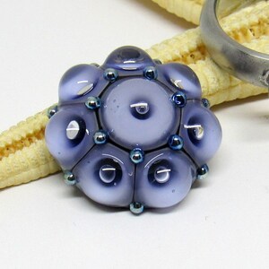 May include: A purple glass bead with a faceted design and silver accents. The bead is made up of multiple smaller circles.