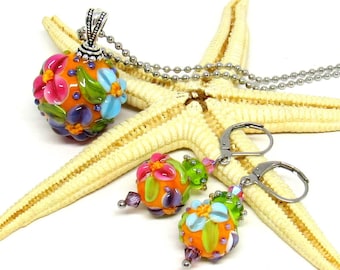May include: A colorful floral necklace and matching earrings set. The necklace features a round pendant with a bright orange background and multi-colored flowers. The earrings are also round with a bright orange background and multi-colored flowers.