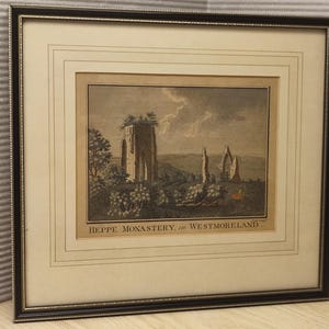 May include: A framed print featuring an etching of Heppe Monastery in Westmoreland. The artwork depicts stone ruins in a landscape with trees and a cloudy sky. The print is housed in a dark brown frame with a cream-colored mat and thin border lines.