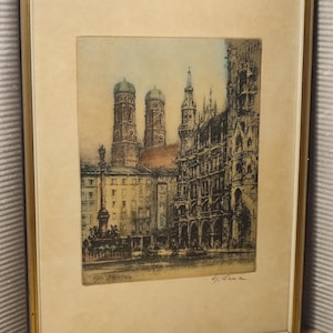 May include: A framed etching depicting a city square with the Frauenkirche in Munich, featuring its two iconic onion-domed towers, a central column monument, and ornate gothic architecture, all rendered in muted sepia and blue tones.