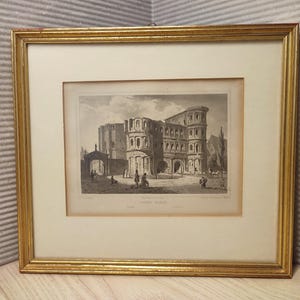 May include: Framed black and white print of a historic building with arched entrances and a tower. The print is set in a gold-coloured wooden frame with a cream-coloured mount.