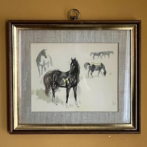 May include: Framed artwork featuring a watercolor painting of a black horse with a flowing mane and tail. The artwork includes several sketched horse figures in the background. The frame is a dark brown with a gold inner edge, and the background is a light gray fabric.