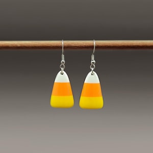 May include: A pair of candy corn earrings. Each earring features a white top, orange middle, and yellow bottom, mimicking the classic Halloween treat. The earrings hang from silver-colored fish hook ear wires, perfect for a festive look.