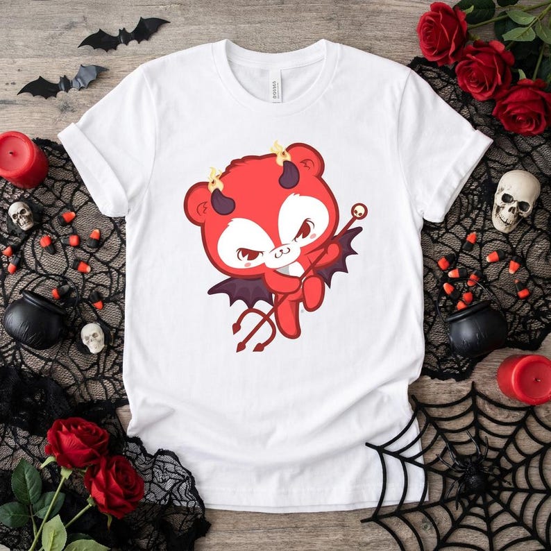 K&ouml;nnte beinhalten: Wei&szlig;es T-Shirt mit einem Cartoon-Teufelsb&auml;ren-Design. Der B&auml;r ist rot mit H&ouml;rnern, Fledermausfl&uuml;geln und einem Dreizack. Das Design ist mittig auf dem T-Shirt platziert, passend f&uuml;r Halloween oder Themenveranstaltungen.