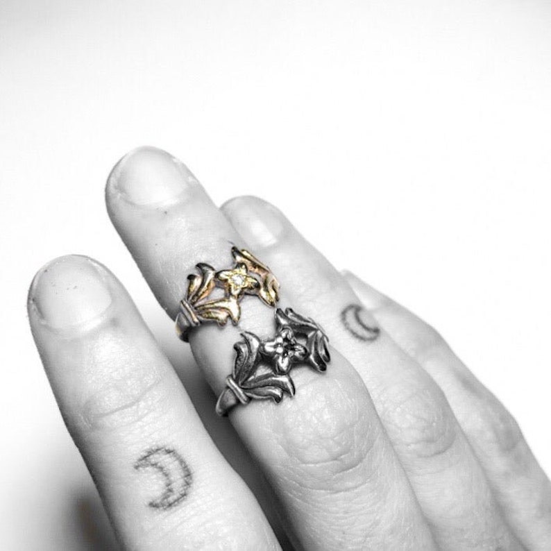 May include: Two silver rings with floral designs. The top ring has a gold flower with a small diamond in the centre.