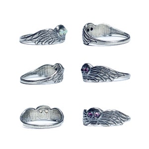 Puede incluir: Cuatro anillos de plata con un dise&ntilde;o de calavera. Dos anillos tienen ojos de gemas rojas, y dos anillos tienen ojos de gemas blancas. Los anillos tienen alas a cada lado de la calavera.
