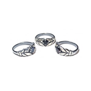 May include: Three silver rings with black gemstones and leaf designs. The rings are arranged in a row on a white background.