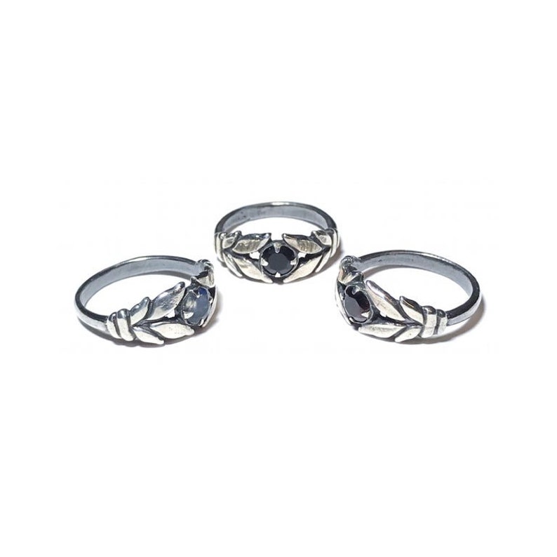 May include: Three silver rings with black gemstones and leaf designs. The rings are arranged in a row on a white background.