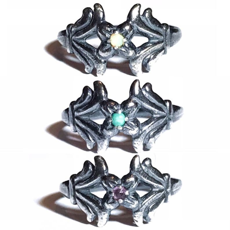 May include: Three silver rings with a floral design. Each ring features a different coloured gemstone in the centre: a pale yellow, a turquoise green, and a purple.