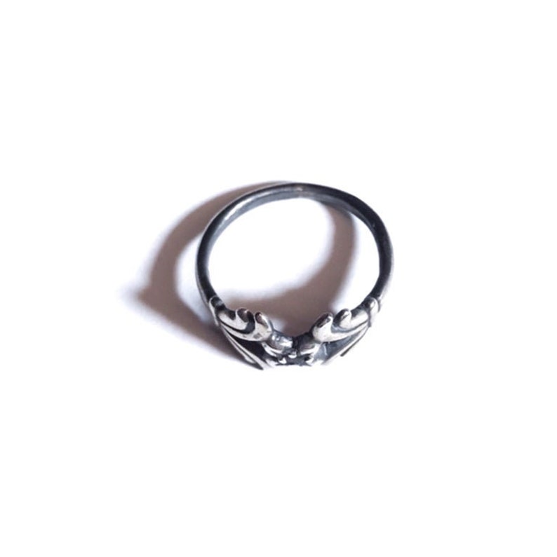 May include: A silver ring featuring a delicate design of two intertwined leaves.