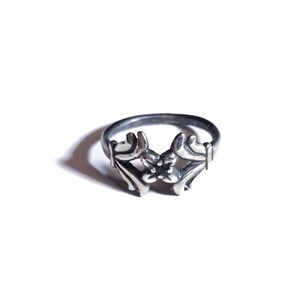 May include: A silver ring featuring a floral design with a black stone at its centre.