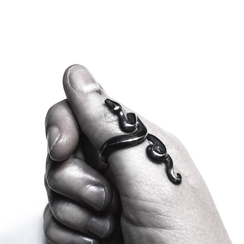 May include: A silver snake ring with a detailed design. The ring is worn on the thumb of a hand.
