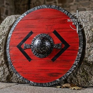 Puede incluir: Un escudo circular de madera con un acabado rojo vibrante y veta de madera visible. El escudo tiene un borde de metal oscuro y texturizado y un umbo central abombado. Acentos geométricos negros flanquean el centro. Texto MEDIEVAL RELIC visible.