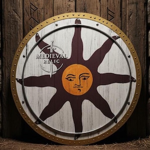 May include: A circular wooden shield featuring a sun design with a face and eight rays. The shield has a gold-coloured rim and is riveted. The text "MEDIEVAL RELIC" is visible. The background is a wooden wall with stone blocks.