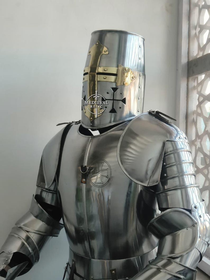 May include: A polished steel suit of armor, including a helmet with brass accents and a cross design. The armor features articulated plates for the arms and legs, and a chest plate with a cross emblem. The text "MEDIEVAL RELIC" is visible on the helmet.