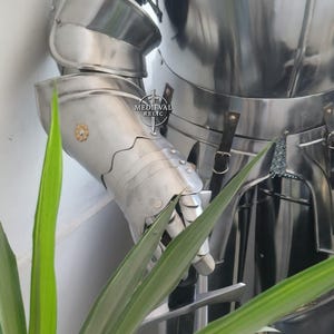 May include: A polished, silver-colored suit of armor, featuring articulated plates for the arms and torso. The armor has a reflective surface and is designed with overlapping segments. The image includes the text "MEDIEVAL RELIC".