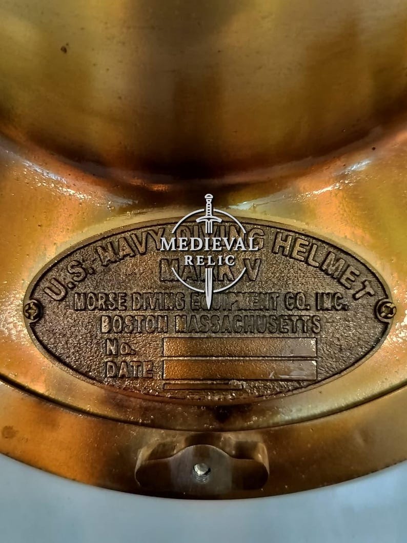 May include: A close-up of a vintage brass U.S. Navy diving helmet. The helmet features an oval plaque with embossed text: "U.S. NAVY DIVING HELMET MARK V" and "MORSE DIVING EQUIPMENT CO. INC. BOSTON MASSACHUSETTS". The helmet is a relic.