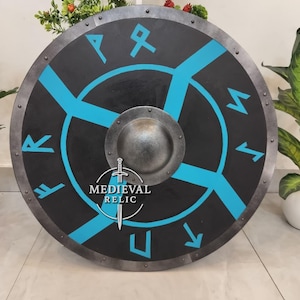 Może przedstawiać: Okrągła, czarna tarcza ze srebrną obwódką i centralnym guzkiem. Posiada niebieski geometryczny wzór i runy. Tarcza zawiera napis "MEDIEVAL RELIC" i logo miecza.