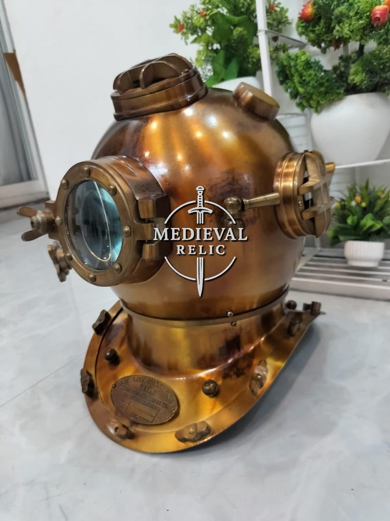 May include: A vintage brass diving helmet with a round, glass-covered viewport and multiple fittings. The helmet has a weathered, antique finish and a base with several bolts. The text "MEDIEVAL RELIC" is visible on the front.