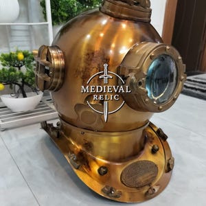 May include: A vintage brass diving helmet with a large front viewing port and side portholes. The helmet has a weathered, antique finish, and a plate with text is visible on the front. The helmet is a decorative item.