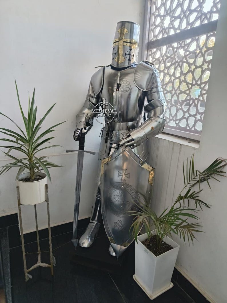 May include: A full suit of polished steel armor, including a helmet with a cross design, stands upright. The armor is complete with a shield and a long sword. The image is of a medieval knight's armor.