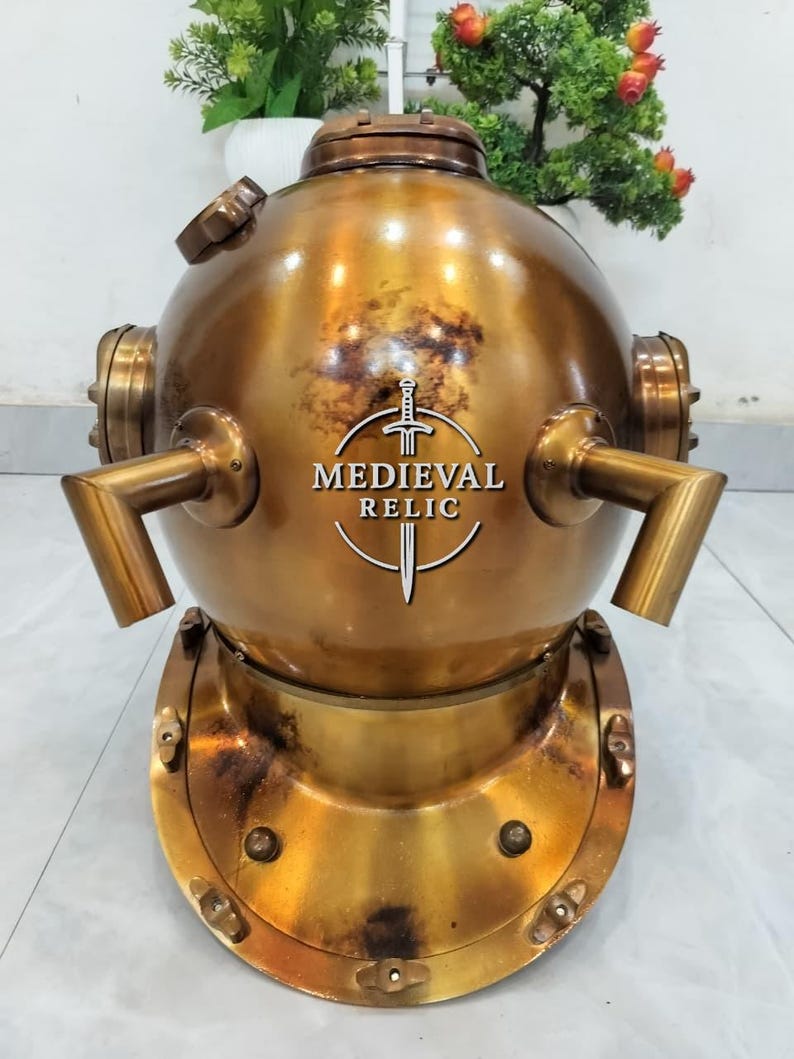 May include: A vintage brass diving helmet with a round top and a wide, bolted base. The helmet has multiple ports and tubes, and the text "MEDIEVAL RELIC" is visible on the front. The brass has a weathered, antique finish.