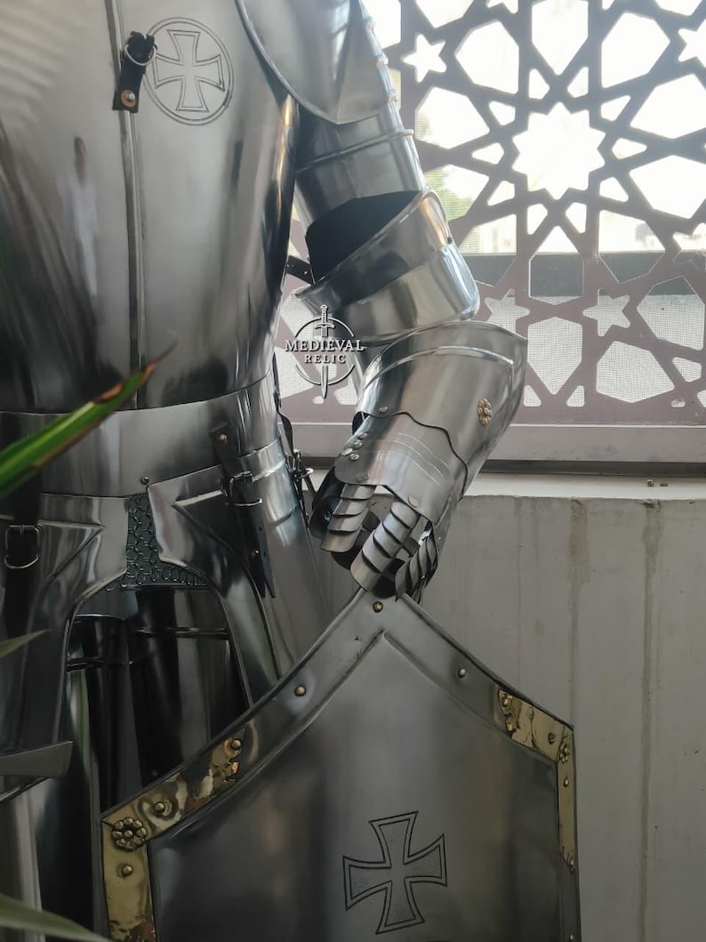 May include: A polished, silver-colored suit of armor with a cross emblem on the chest plate and a gauntlet. The armor is highly reflective, with visible rivets and intricate joint details. The image includes the text "MEDIEVAL RELIC".